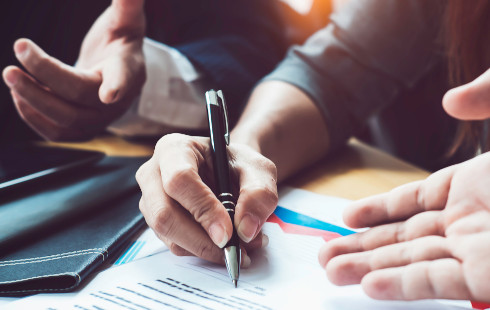 A view of two persons hands with one signing a contract